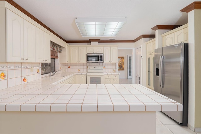 kitchen with ornamental molding, stainless steel appliances, tile counters, and kitchen peninsula