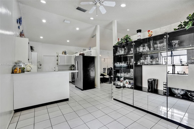 kitchen with vaulted ceiling, stainless steel fridge, light tile patterned floors, and white cabinets