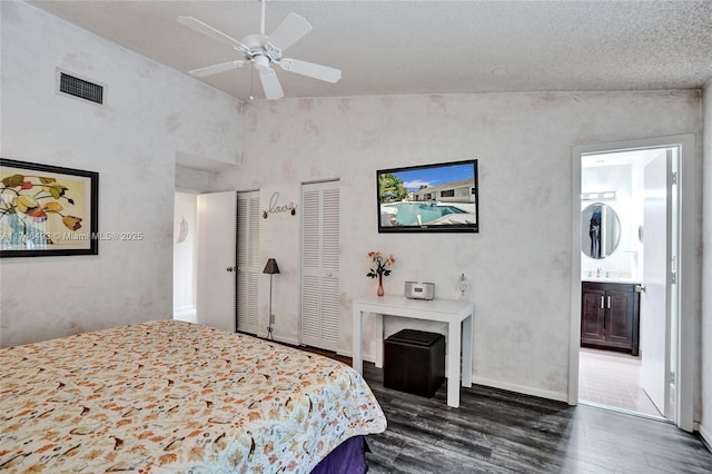 bedroom featuring dark hardwood / wood-style flooring, connected bathroom, multiple closets, and ceiling fan