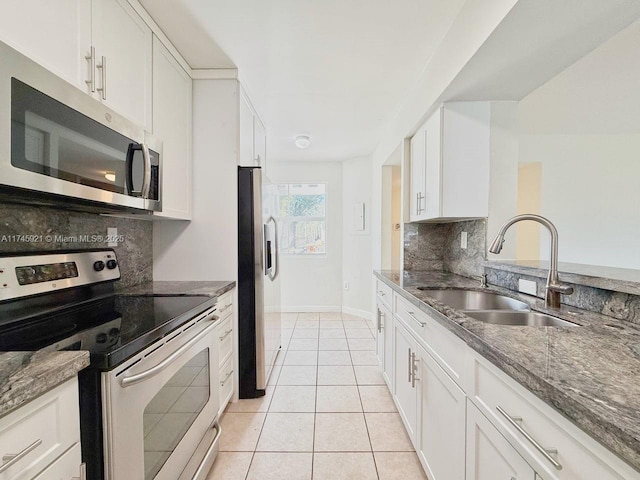 kitchen with sink, light tile patterned floors, white cabinetry, stainless steel appliances, and dark stone counters