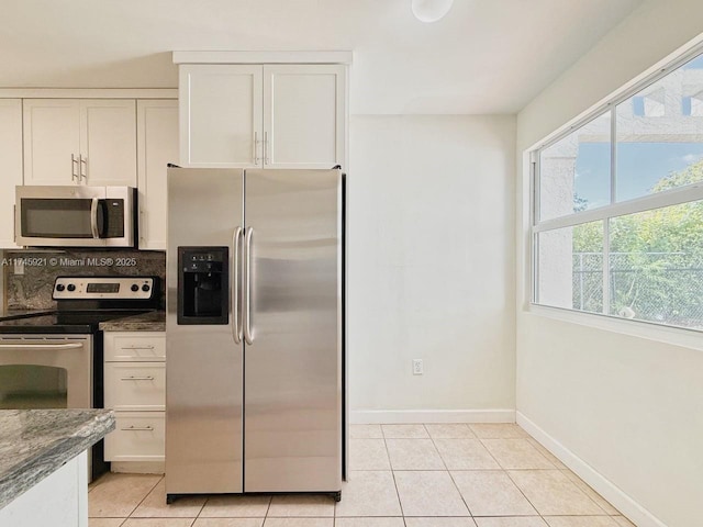 kitchen featuring stainless steel appliances, dark stone countertops, white cabinets, and light tile patterned floors