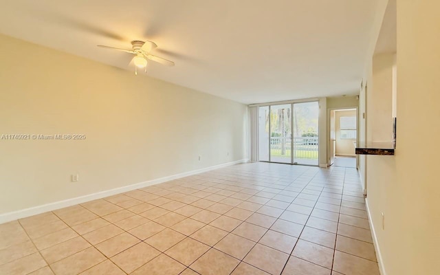 tiled spare room featuring ceiling fan and a wall of windows