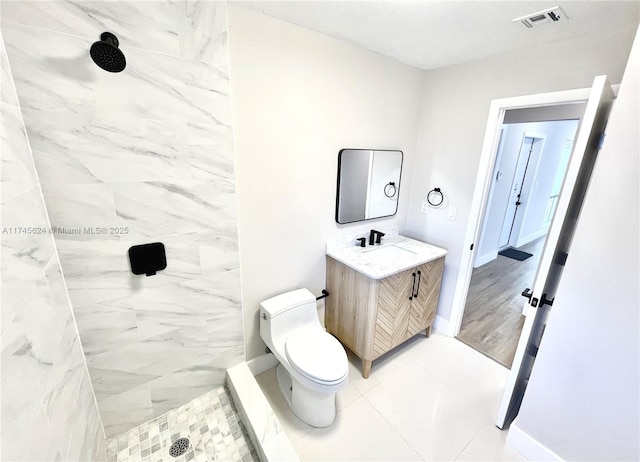 bathroom with tile patterned flooring, vanity, a tile shower, and toilet