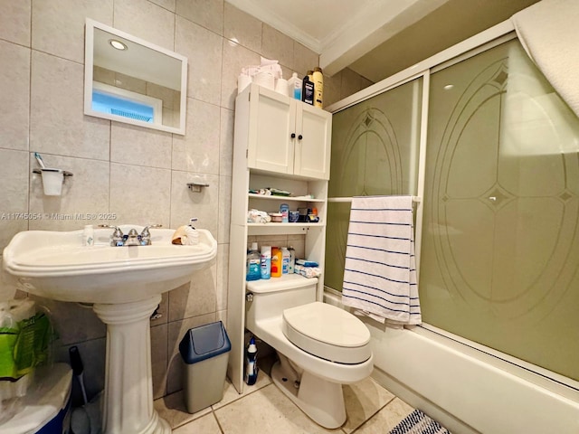 bathroom featuring tile patterned floors, toilet, combined bath / shower with glass door, and tile walls