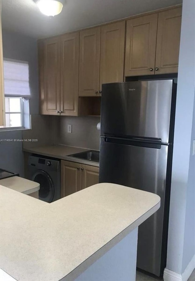 kitchen featuring light countertops, washer / clothes dryer, light brown cabinets, and freestanding refrigerator