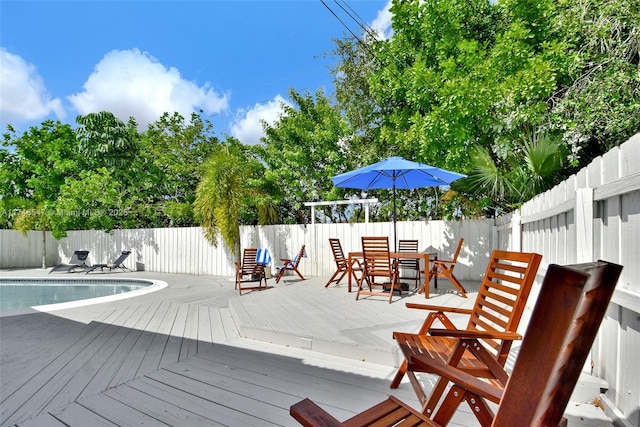 wooden terrace with outdoor dining space, fence, and a fenced in pool