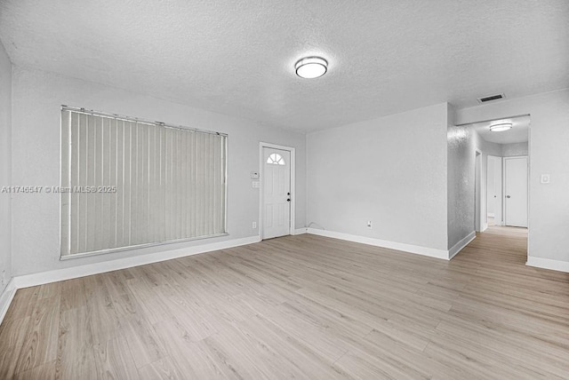 spare room featuring light wood-style floors, visible vents, a textured ceiling, and baseboards