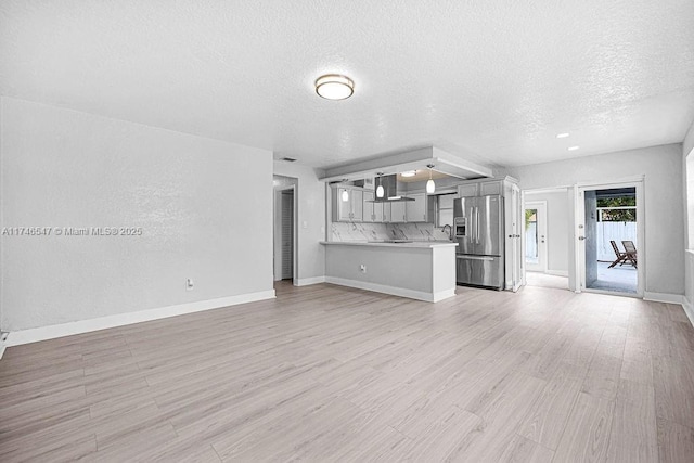 unfurnished living room with light wood-type flooring, baseboards, and a textured ceiling