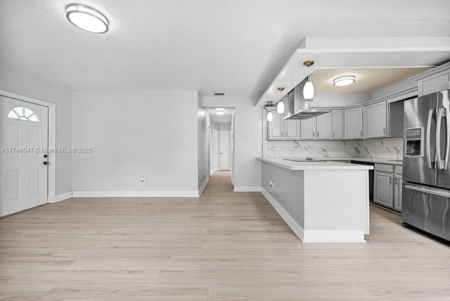 kitchen with decorative backsplash, gray cabinetry, light wood-style floors, stainless steel fridge, and a peninsula