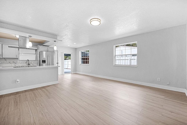 unfurnished living room with baseboards, a sink, light wood-style flooring, and a healthy amount of sunlight