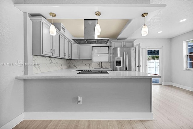 kitchen with island exhaust hood, stainless steel refrigerator with ice dispenser, light countertops, gray cabinetry, and a peninsula