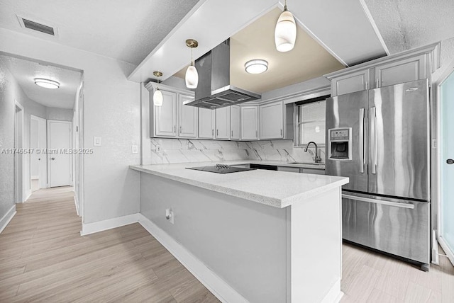 kitchen featuring black electric stovetop, visible vents, a sink, island range hood, and stainless steel fridge