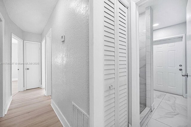 corridor with marble finish floor, a textured wall, visible vents, and baseboards