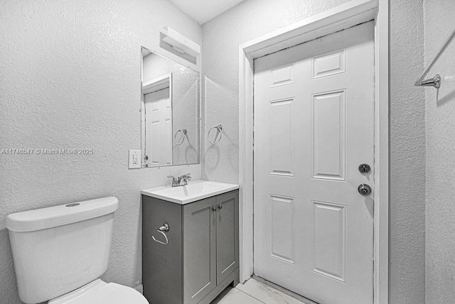 half bath with marble finish floor, a textured wall, vanity, and toilet