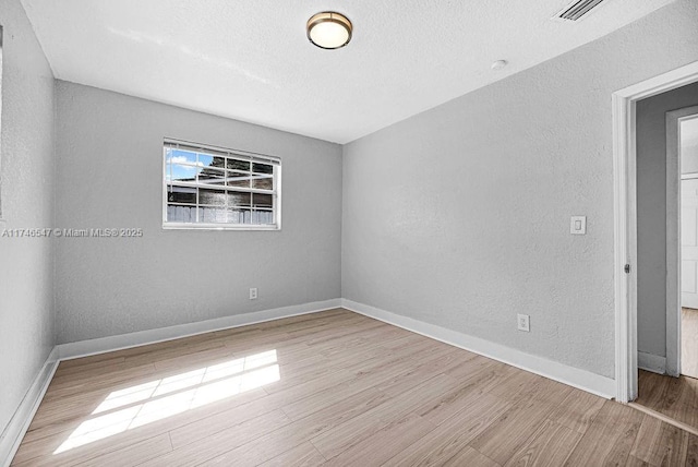 spare room featuring baseboards, wood finished floors, and a textured wall