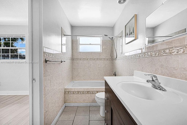 bathroom featuring tile walls, toilet, tiled shower / bath combo, vanity, and tile patterned flooring