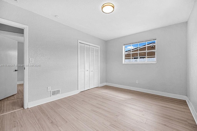 unfurnished bedroom with a textured wall, wood finished floors, visible vents, baseboards, and a closet