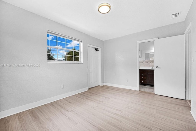 empty room with light wood finished floors, visible vents, and baseboards