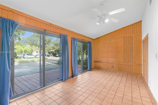 empty room featuring vaulted ceiling, light tile patterned flooring, ceiling fan, and wood walls