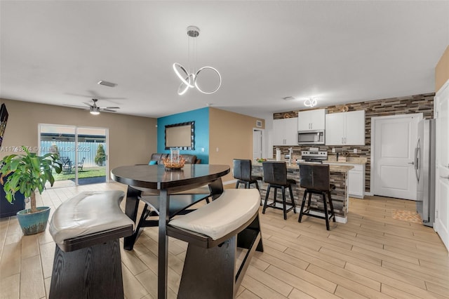 dining room with ceiling fan with notable chandelier and light hardwood / wood-style flooring