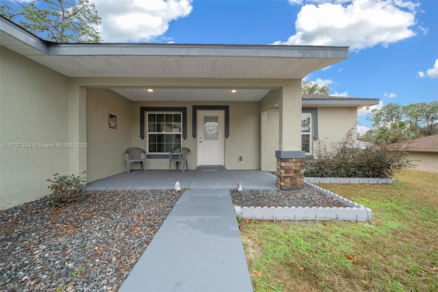 property entrance featuring covered porch, a lawn, and stucco siding