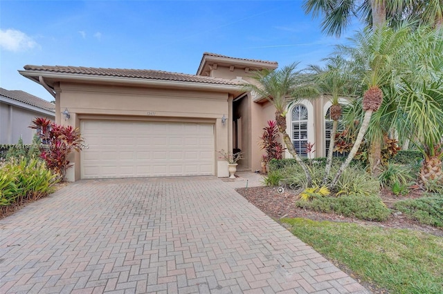 mediterranean / spanish house with a garage, a tiled roof, decorative driveway, and stucco siding