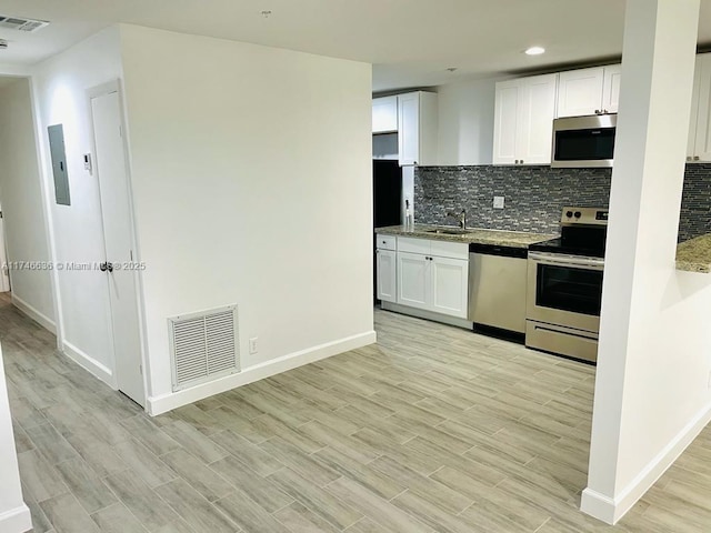 kitchen featuring tasteful backsplash, light stone counters, light wood-type flooring, appliances with stainless steel finishes, and white cabinets