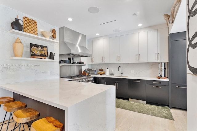 kitchen with range, wall chimney exhaust hood, a peninsula, open shelves, and a sink