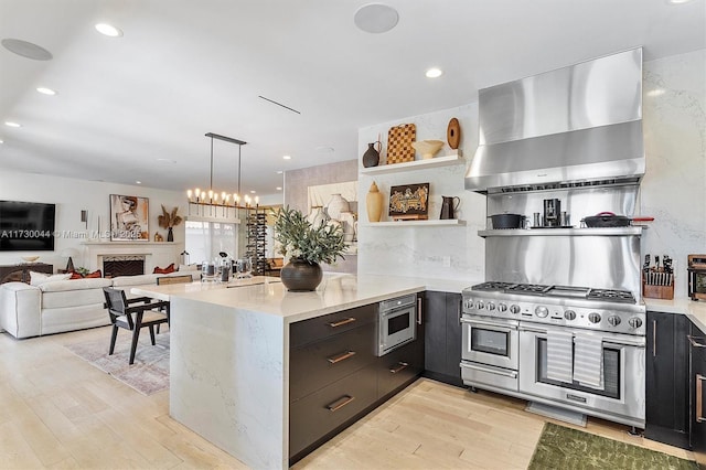 kitchen with range with two ovens, a peninsula, wall chimney range hood, open shelves, and light wood finished floors