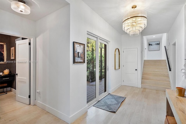 foyer entrance featuring baseboards, a notable chandelier, light wood finished floors, and stairs