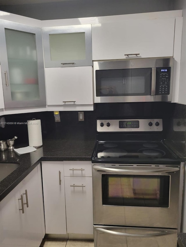 kitchen with glass insert cabinets, white cabinetry, appliances with stainless steel finishes, and dark stone counters