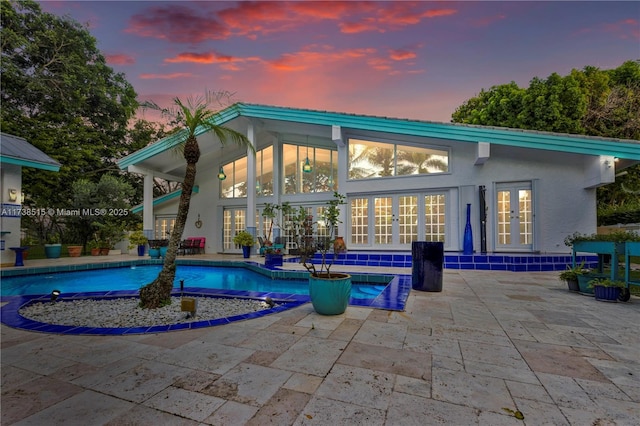 pool at dusk with french doors, a hot tub, and a patio