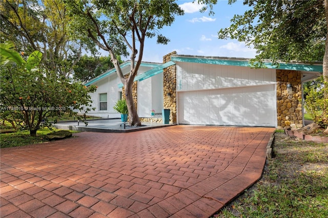 view of front of property featuring decorative driveway, stone siding, and a garage