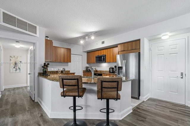 kitchen with a breakfast bar area, dark stone countertops, dark hardwood / wood-style floors, stainless steel fridge, and kitchen peninsula