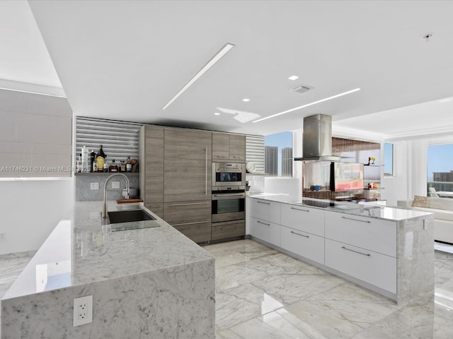 kitchen with double oven, white cabinetry, sink, island exhaust hood, and light stone counters