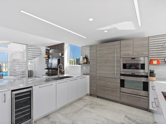 kitchen featuring sink, white cabinetry, double oven, beverage cooler, and light stone countertops