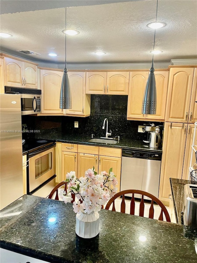 kitchen with sink, appliances with stainless steel finishes, a textured ceiling, decorative light fixtures, and dark stone counters