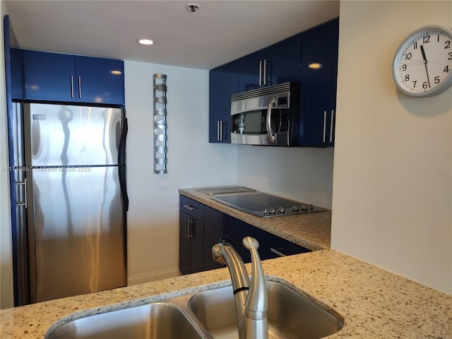 kitchen with blue cabinetry, stainless steel appliances, sink, and light stone counters