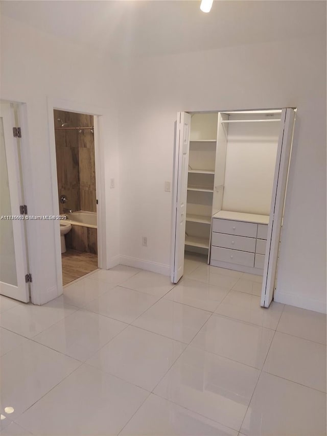 unfurnished bedroom with light tile patterned floors, a walk in closet, a closet, and ensuite bathroom