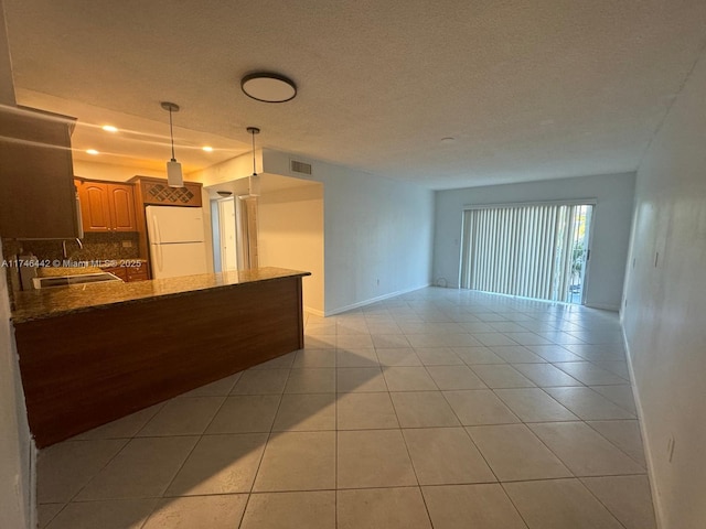 kitchen with dark stone counters, hanging light fixtures, white fridge, light tile patterned floors, and kitchen peninsula