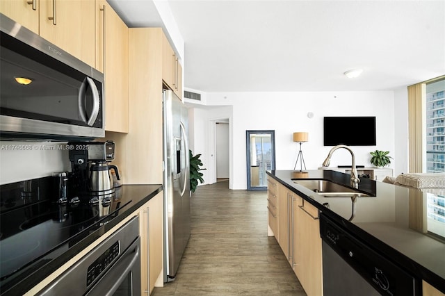 kitchen with dark countertops, light brown cabinets, appliances with stainless steel finishes, and a sink