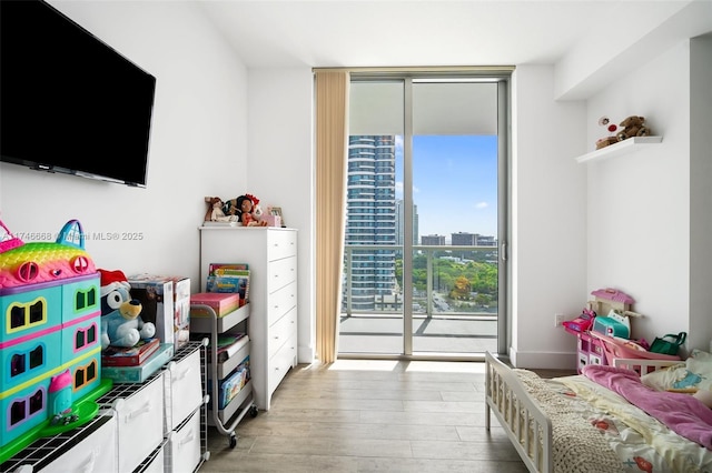 bedroom featuring a wall of windows, a view of city, access to exterior, and light wood finished floors