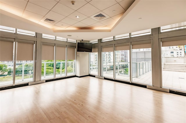 empty room with light wood-type flooring, a towering ceiling, visible vents, and a paneled ceiling