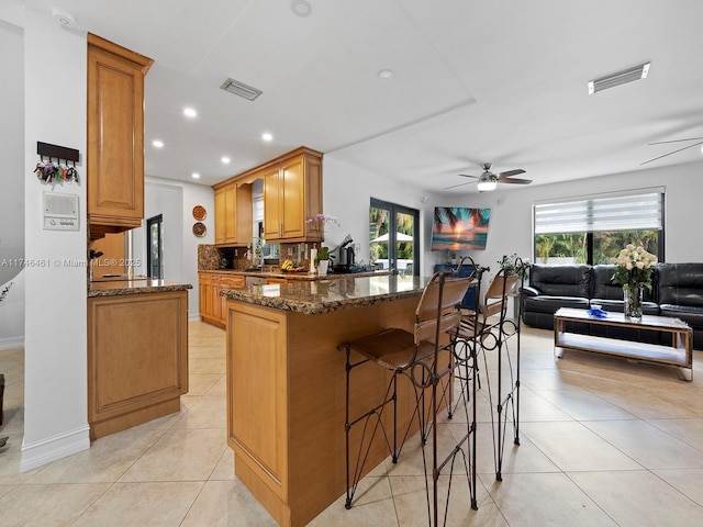 kitchen with light tile patterned flooring, a kitchen breakfast bar, dark stone counters, and kitchen peninsula