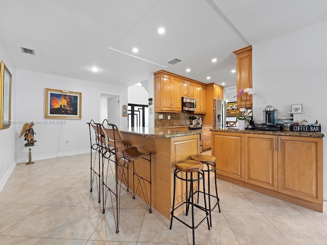 kitchen with dark stone countertops, light tile patterned floors, stainless steel appliances, and kitchen peninsula