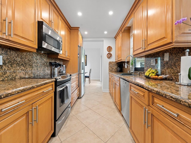 kitchen featuring appliances with stainless steel finishes, light tile patterned flooring, sink, and dark stone counters