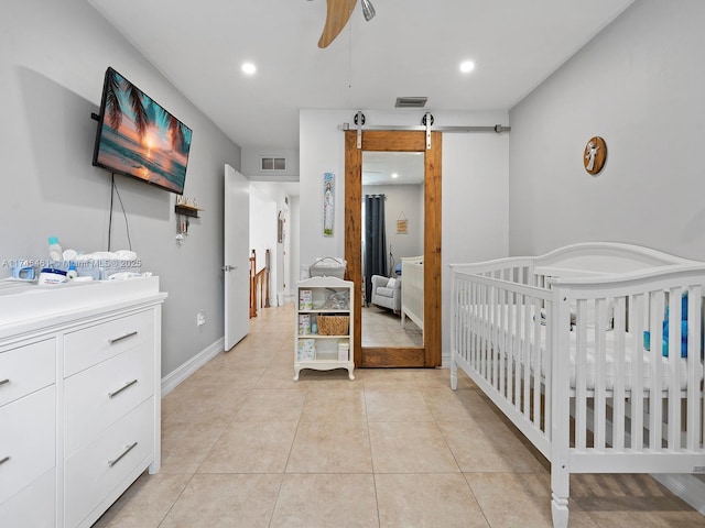 bedroom with a crib, light tile patterned floors, ceiling fan, and a barn door