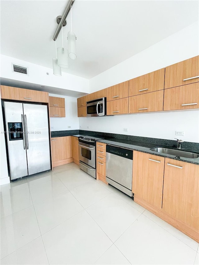 kitchen with sink, hanging light fixtures, dark stone countertops, light tile patterned floors, and appliances with stainless steel finishes