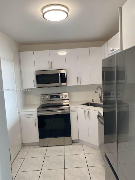 kitchen featuring white cabinetry, sink, light tile patterned floors, and appliances with stainless steel finishes