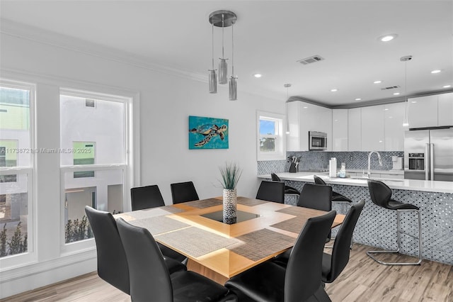 dining area with sink, crown molding, and light hardwood / wood-style floors